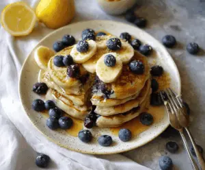 Delicious fluffy vegan blueberry pancakes stacked on a plate, topped with fresh blueberries and syrup.